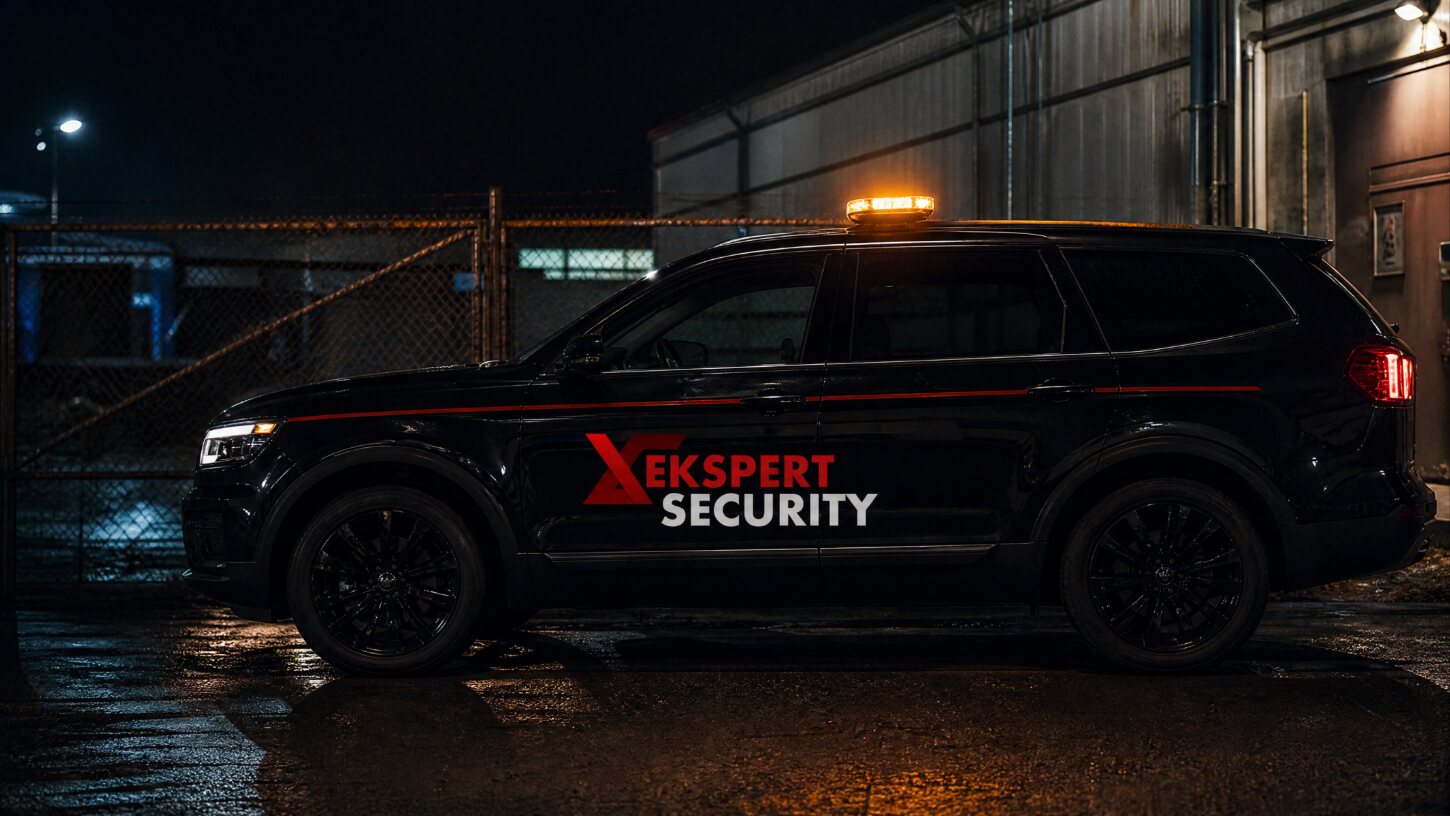 Czarny radiowóz Ekspert Security z logo na drzwiach przy bramie zakładu nocą
